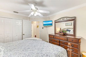 A bedroom with a bed, dresser, ceiling fan, and a wall-mounted TV.