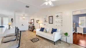 A spacious living area with a white sofa, a dining table, chairs, a ceiling fan, and a small side table with a lamp. - Coral Princess Waterfront Pool & Hot Tub (Cape Coral)