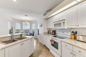 A kitchen with white cabinets, a stainless steel sink, a microwave, a stove, and a toaster. - Coral Princess Waterfront Pool & Hot Tub (Cape Coral)