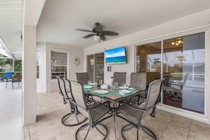 A dining area with a table set for four, chairs, a ceiling fan, and a TV mounted on the wall.