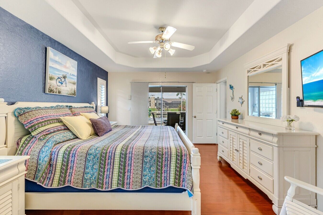 Een slaapkamer met een bed, een plafondventilator, een dressoir en een groot raam.