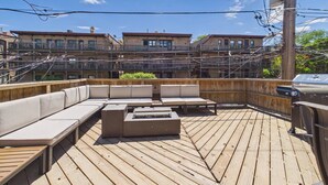 Terraza en la azotea con mobiliario exterior, una parrilla y vistas a edificios de varios pisos.