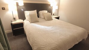 Hotellihuone, jossa on suuri sänky, kaksi yöpöytää ja kaksi seinään kiinnitettyä lamppua.