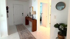 A hallway with a white door, a wooden bench, a lamp, a clock, and a plant. - Jax Waterfront Retreat at Winchester Ridge (Jacksonville)