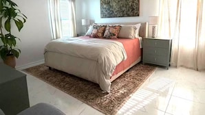 A bedroom with a bed, a ceiling fan, a nightstand, a lamp, a potted plant, and a window with curtains. - Jax Waterfront Retreat at Winchester Ridge (Jacksonville)