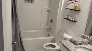 A bathroom with a bathtub, toilet, marble floor, and a shower curtain. - Jax Waterfront Retreat at Winchester Ridge (Jacksonville)