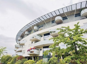 A multi-story building with balconies, large windows, and a curved roof structure.