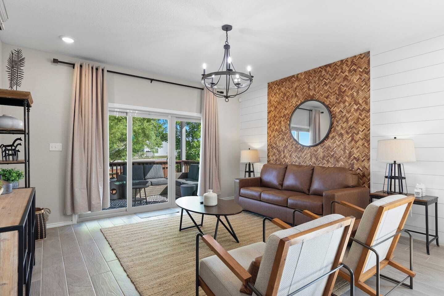 A modern living room with a sofa, chairs, a chandelier, and a large window.