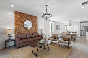 En moderne stue med sofa, stole, et sofabord og en lysekrone.