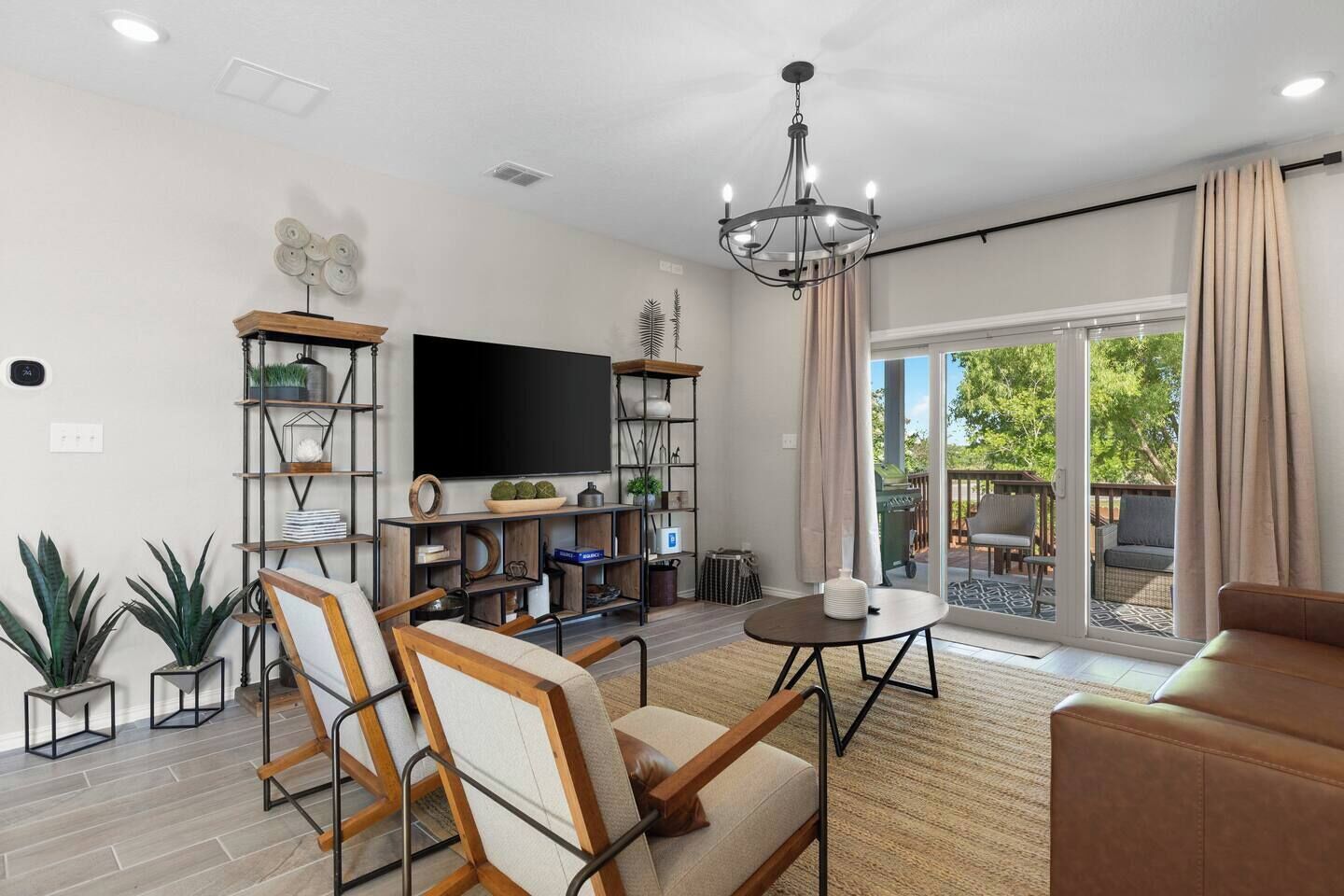 A spacious living room with a flat-screen TV, wooden furniture, and a large sliding glass door leading to an outdoor patio.