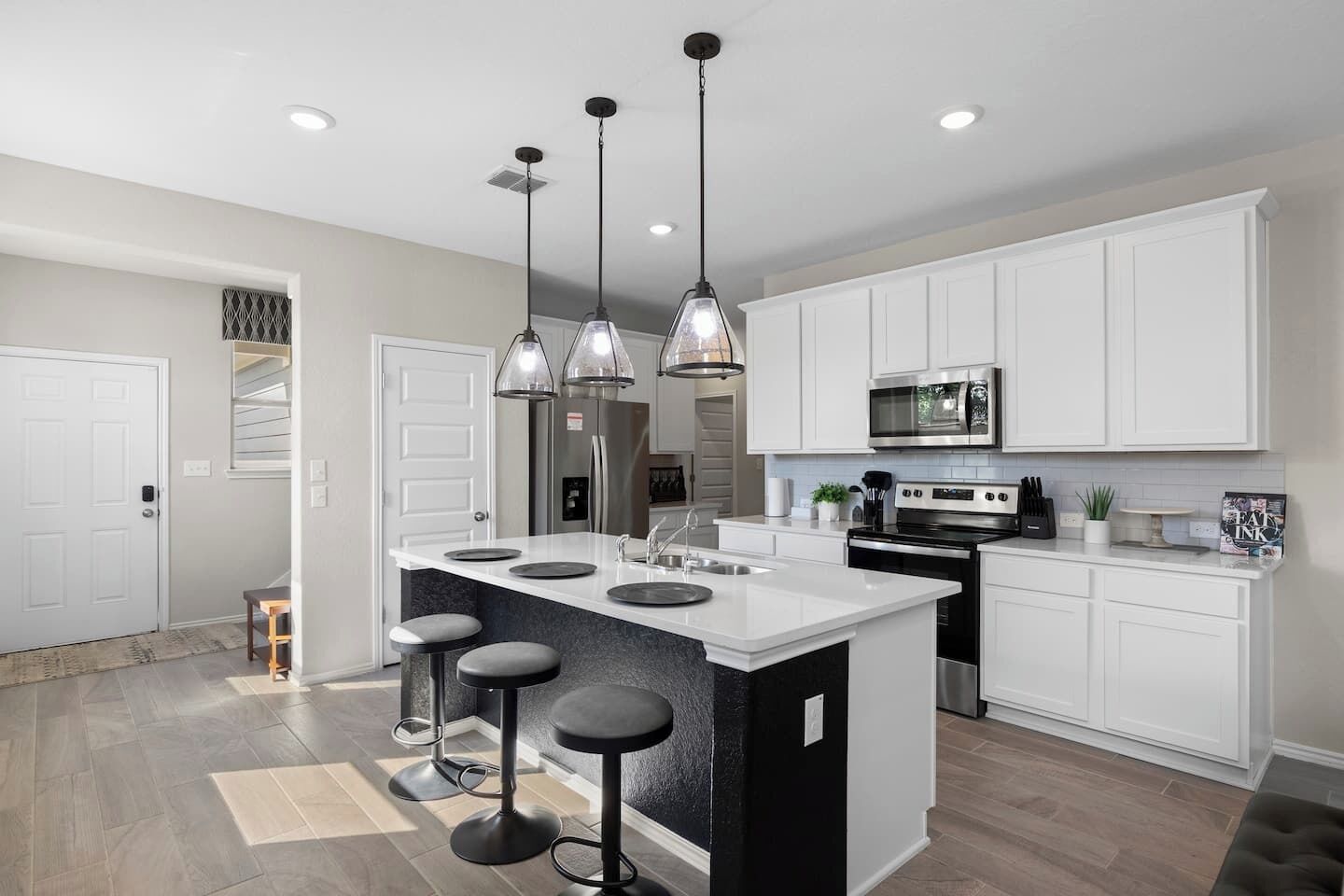 A modern kitchen with a central island, pendant lights, white cabinetry, and a stainless steel range hood.
