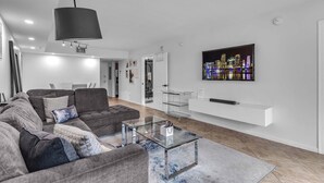 A modern living room with a sectional sofa, a glass coffee table, a mounted TV, and a cityscape artwork. - Brickell Bay View Pool & Gym (Miami)