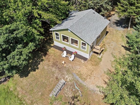 A single-story house with a sloped roof, surrounded by dense trees. - Camp Avaliz - Ocean-view for 2 with a queen bedroom, kitchenette, Wi-Fi and AC (Gouldsboro)