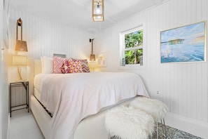 A bedroom with a bed, bedside lamps, a window with a view, and a painting on the wall. - Camp Avaliz - Ocean-view for 2 with a queen bedroom, kitchenette, Wi-Fi and AC (Gouldsboro)