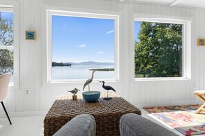 Una habitación con vista a un lago, dos pájaros sobre una mesa y un banco de mimbre.