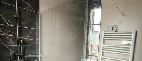 A modern bathroom with a glass shower enclosure, a white towel rack, and a view of the outside through a window.