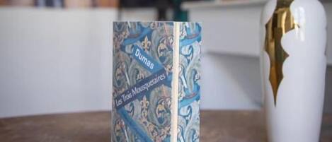 A book titled 'Dumas Les Trois Mousquetaires' on a table with a vase of flowers.