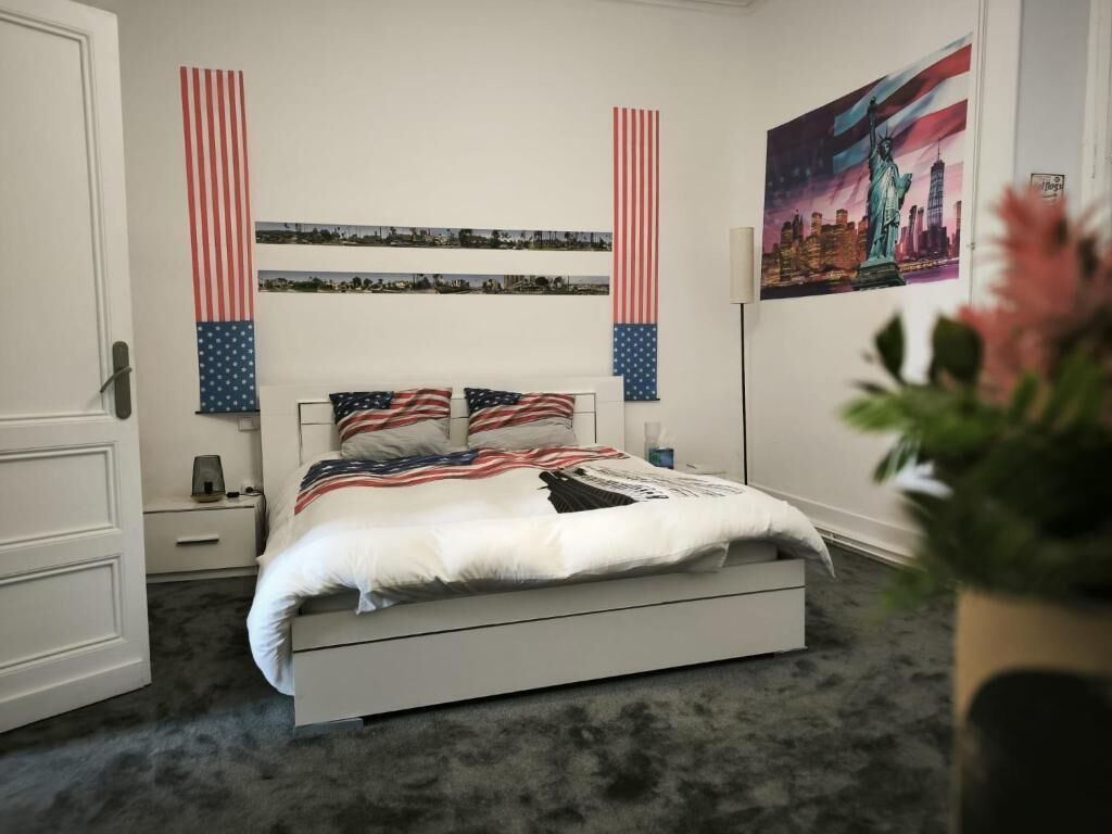 Une chambre à coucher avec un lit, une table de chevet, une étagère fixée au mur et un tableau encadré.