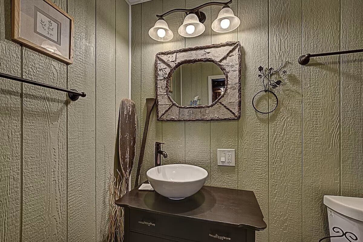 Een badkamer met een rustieke inrichting, bestaande uit een houten wastafelmeubel, een witte wasbak en een spiegel met een verweerde lijst.