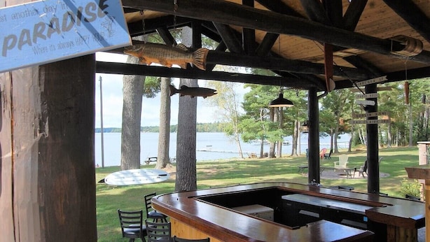 Zona de bar al aire libre techada con vistas a un lago, vigas de madera y un letrero que dice 'PARADISE'.