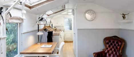 A compact room with a wooden desk, a leather chair, a clock on the wall, and a skylight.