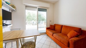 A room with a sofa, a table, chairs, a TV, and a balcony with a view. - GuestHost - Cozy Balcony Apartment with Ocean View (Pineto)