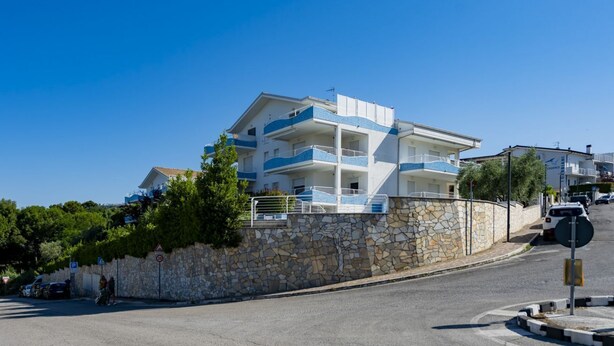 A multi-story building with balconies, a stone wall, and a clear blue sky. - GuestHost - Cozy Balcony Apartment with Ocean View (Pineto)