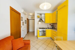 A compact kitchen with yellow cabinets, a wooden table, and a sofa. - GuestHost - Cozy Balcony Apartment with Ocean View (Pineto)