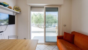 A modern living room with a wooden table, a sofa, a TV mounted on the wall, and a sliding glass door leading to an outdoor area. - GuestHost - Cozy Balcony Apartment with Ocean View (Pineto)