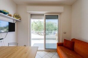 Ein modernes Wohnzimmer mit Holztisch, einer Couch, einem an der Wand befestigten Fernseher und einer Schiebetür zu einem Außenbereich.