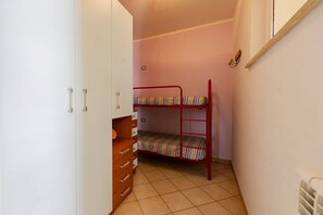 Ein schmales Zimmer mit einem Etagenbett, einem Schrank mit Schubladen und einer Heizung.