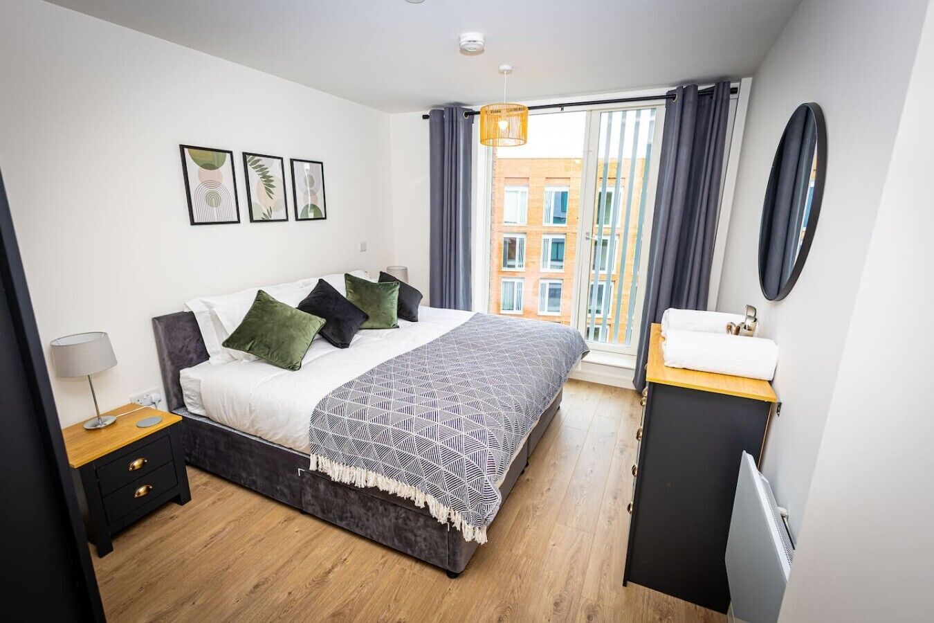 A modern bedroom with a bed, bedside table, and a view of buildings through the window.