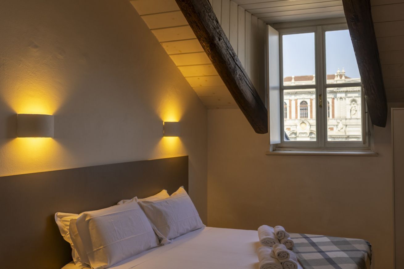 Una camera da letto con un letto, due luci a parete, una finestra e vista su un edificio.