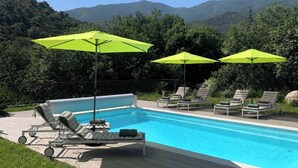 A swimming pool with lounge chairs and bright green umbrellas, surrounded by greenery and hills. - Les Albères Bed & Breakfast Suite with a view of the pool and terrace (Villelongue-dels-Monts)