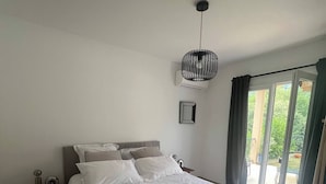 A bedroom with a bed, a nightstand, a hanging light fixture, and a view through a glass door. - Les Albères Bed & Breakfast Suite with a view of the pool and terrace (Villelongue-dels-Monts)