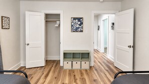 A room with a wooden floor, a white door, a bench with storage drawers, and a framed picture on the wall. - Cozy 2 Bedroom Monthly (Hot Springs)