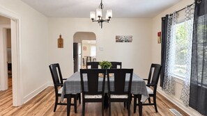 A dining room with a table set for four, surrounded by chairs, a chandelier, and a window with curtains. - Cozy 2 Bedroom Monthly (Hot Springs)