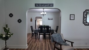 Een eetgedeelte met een tafel voor vier personen, een kroonluchter en een bord boven de deur.