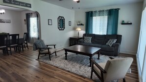 Een woonkamer met een bank, salontafel, stoelen, vloerkleed, lamp en een spiegel aan de muur.