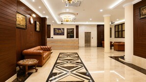 A hotel lobby with a reception desk, leather seating, a patterned carpet, and a chandelier.
