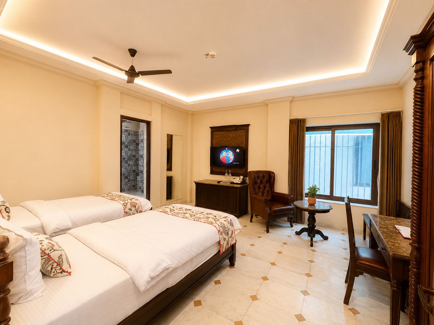 A hotel room with a large bed, a desk, a chair, a television, and a ceiling fan.