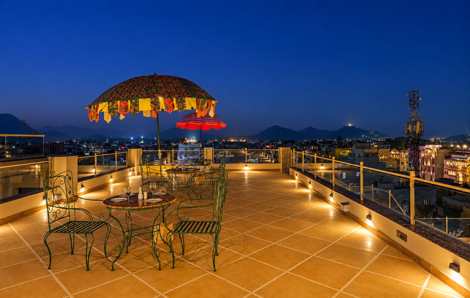 Terraza en la azotea con mobiliario exterior, un parasol decorativo y vistas a la ciudad al anochecer.