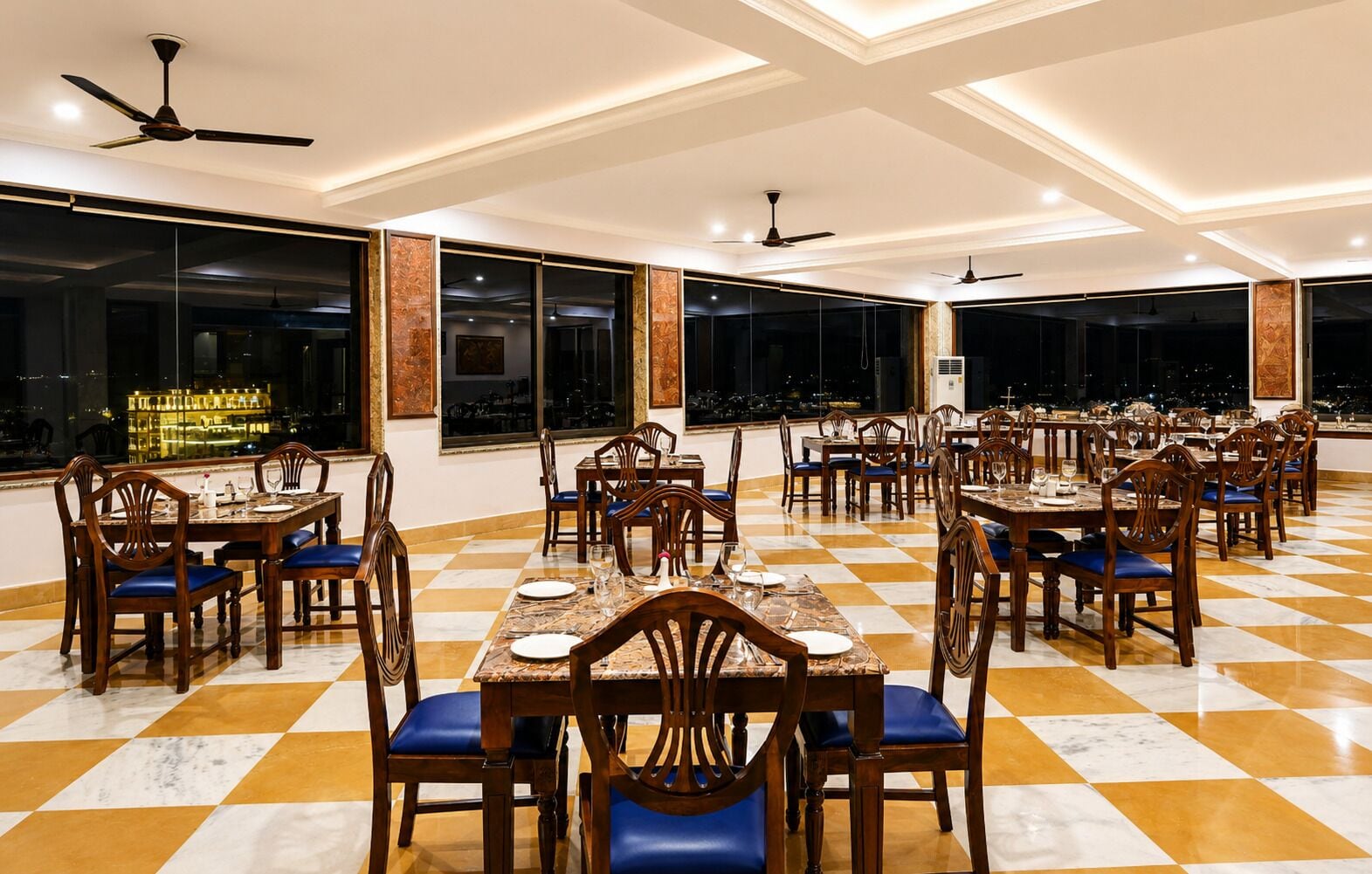 A spacious dining area with multiple tables and chairs, large windows, and ceiling fans.