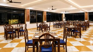 A spacious dining area with multiple tables and chairs, large windows, and ceiling fans. - Barliyas Heritage Boutique Hotel (Udaipur)