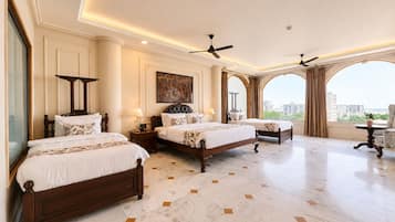 Quarto de hotel com duas camas, uma janela grande e vista para a cidade, e um ventilador de teto.