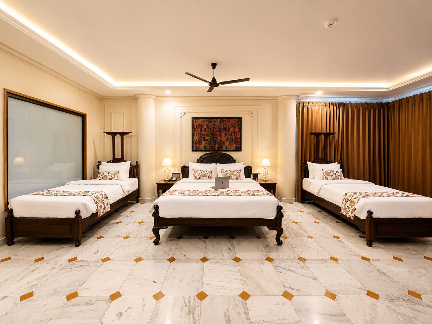 A hotel room with a large bed, two smaller beds, a ceiling fan, a painting, and a large window.