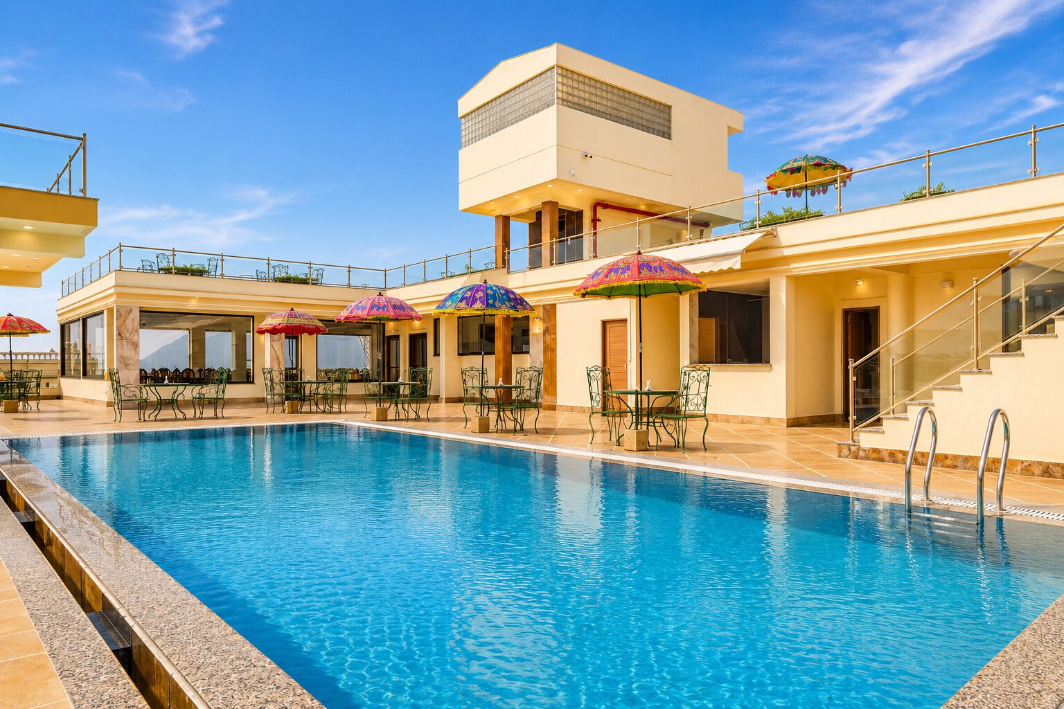 Una piscina con sillones de descanso y sombrillas, un espacio de estar techado y un edificio con balcón.