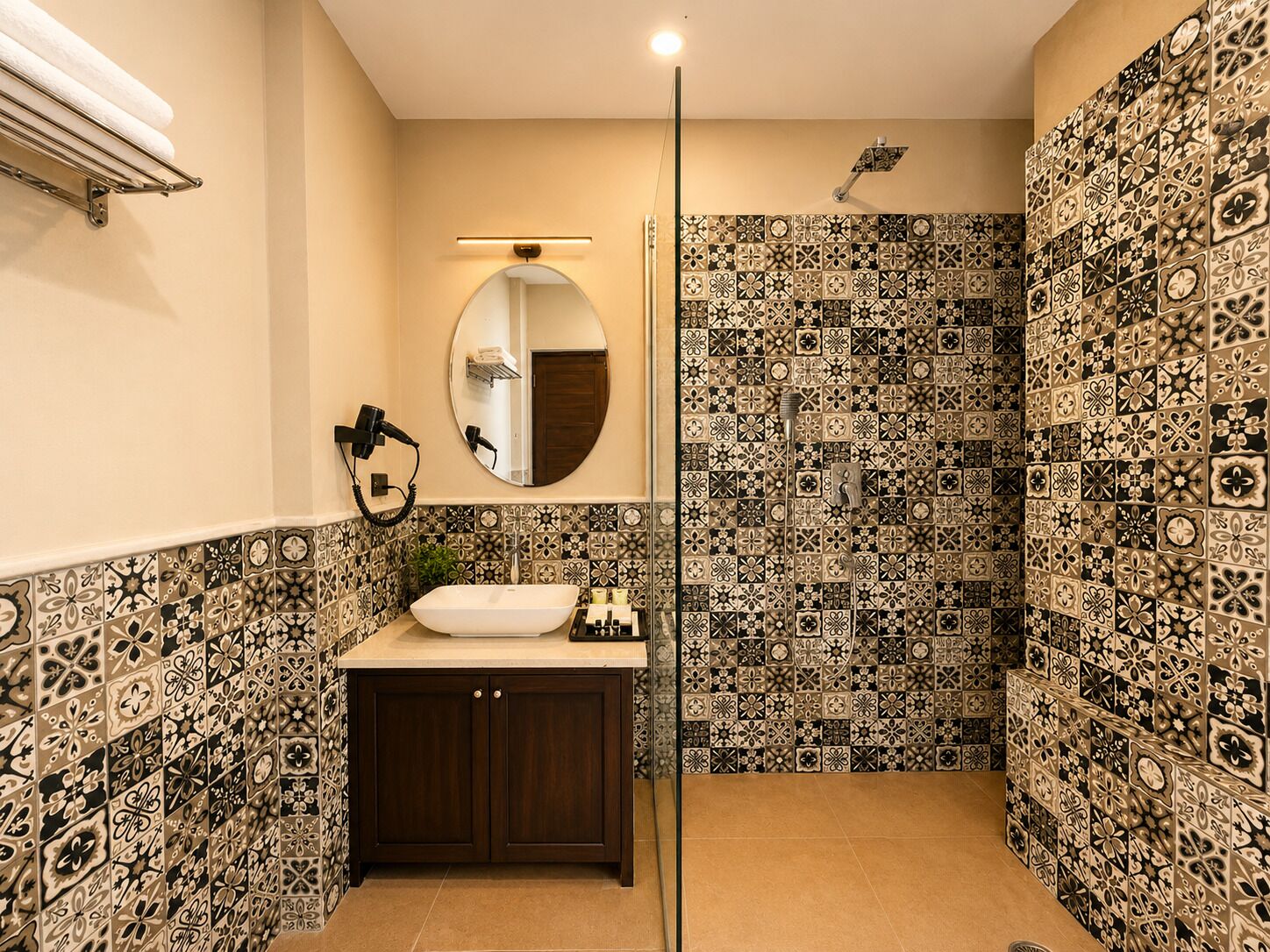 Un baño con un lavabo blanco, armarios de madera oscura, un espejo redondo y una ducha con azulejos estampados.