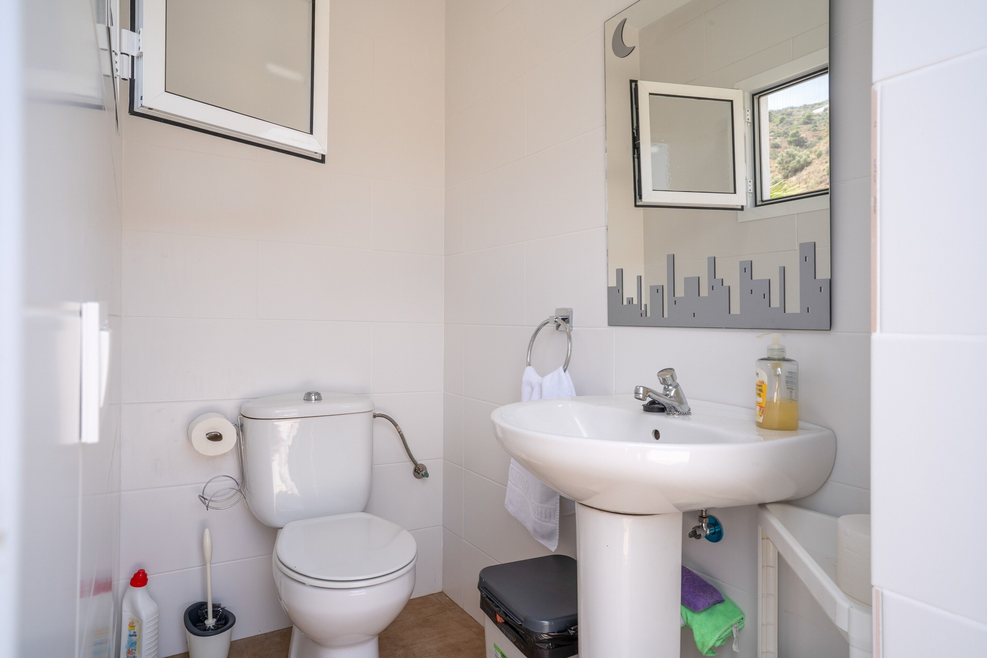 Un baño con inodoro, lavamanos y espejo decorado con un diseño de paisaje urbano.