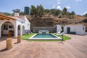 Un espace piscine agrémenté d’un mur en pierre, de chaises longues et d’un petit bâtiment avec une porte verte.